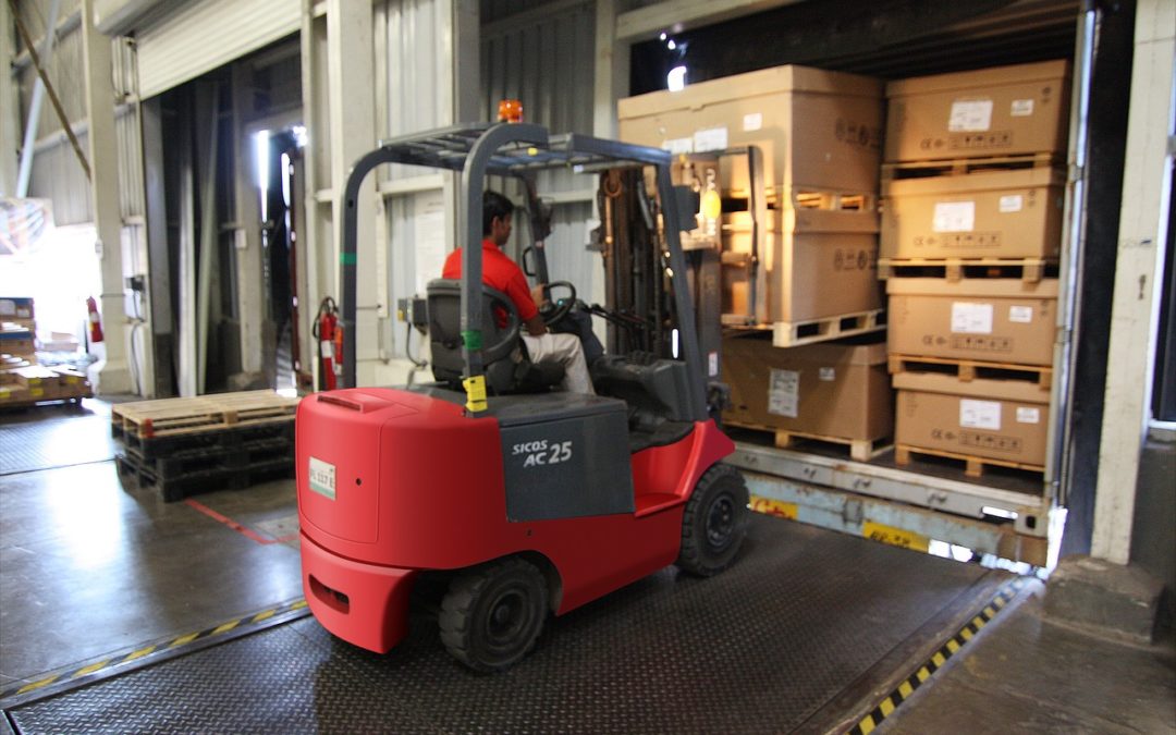 Worker lifts pallets in warehouse with machine.